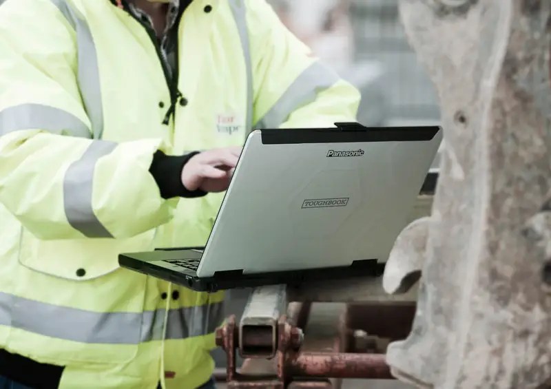 A technician in a high-visibility jacket working on a Panasonic Toughbook outdoors